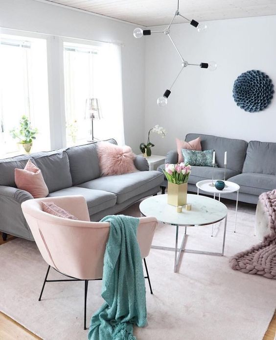 a catchy living room with grey sofas, pink pillows and a chair, coffee tables, a catchy bulb chandelier