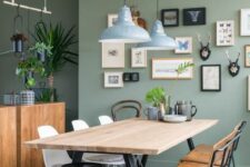 a catchy mid-century modern dining space with sage green walls, a dining table and mismatching chairs, a gallery wall and pendant lamps