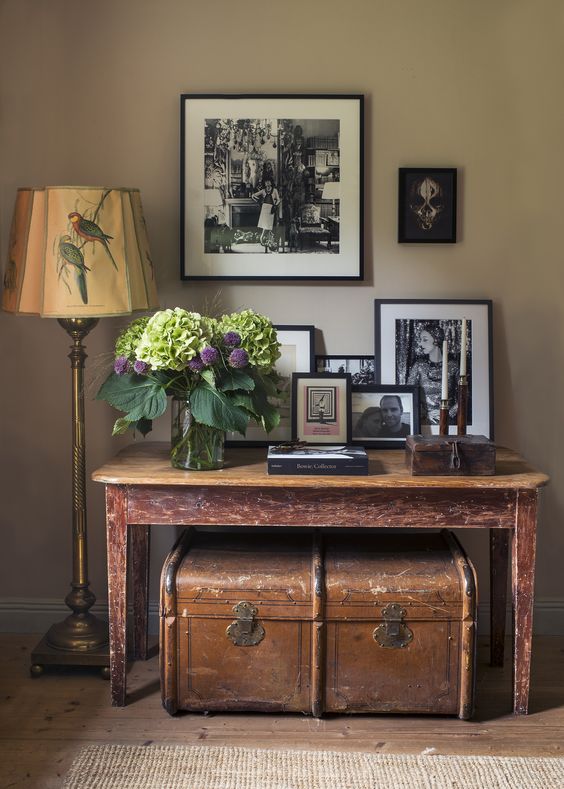 a catchy nook with a beige wall, a shabby chic console table, a vintage trunk, a vintage floor lamp and black and white photos