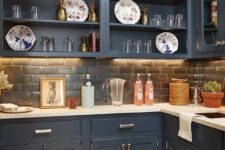 a cathcy navy kitchen with shaker and open cabinets, a brick backsplash and white countertops, elegant gold and brass decor