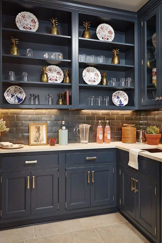 a cathcy navy kitchen with shaker and open cabinets, a brick backsplash and white countertops, elegant gold and brass decor
