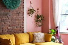 a cheerful living room with a brick and pink wall, a yellow sectional, jute ottomans and greenery is amazing