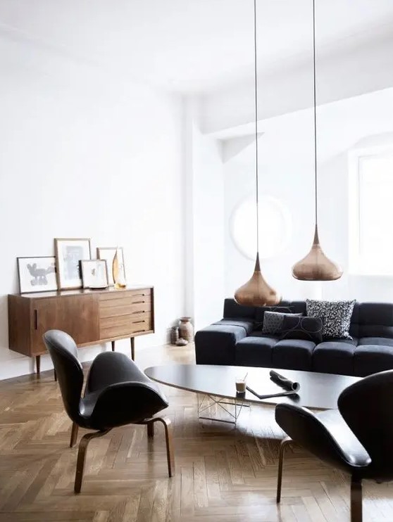 a chic Nordic living room with a black sofa and chairs, an oval coffee table, a stained sideboard and copper pendant lamps