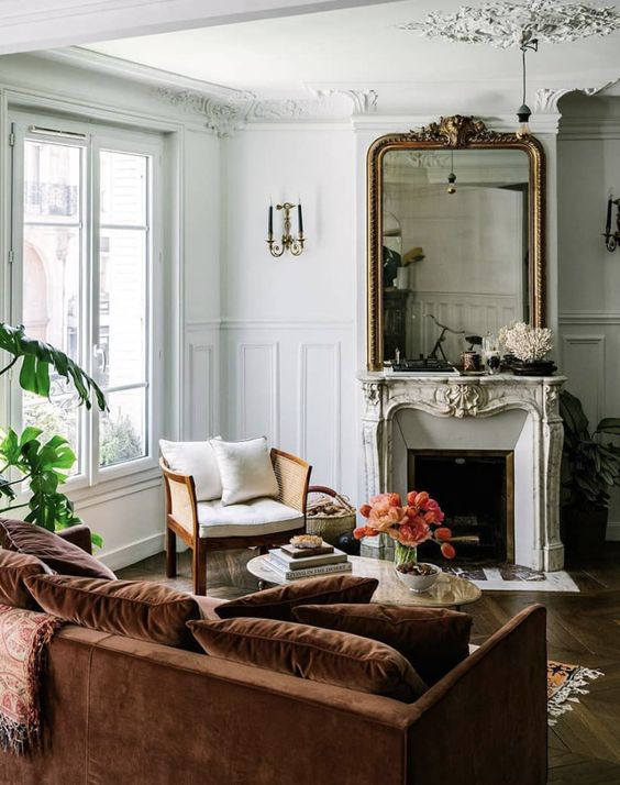 a chic Parisian living room with a French fireplace, a brown velvet sofa, a rattan chair, a coffee table, potted greenery