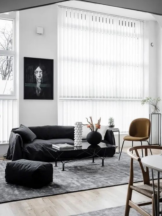 a chic Scandi living room with a black sofa and a pouf, a rust chair and a glass coffee table and some plants