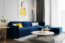 a chic and beautiful living room with dove grey walls, a navy sofa, round tables, a grey pouf, a lovely gold chandelier and some touches of yellow