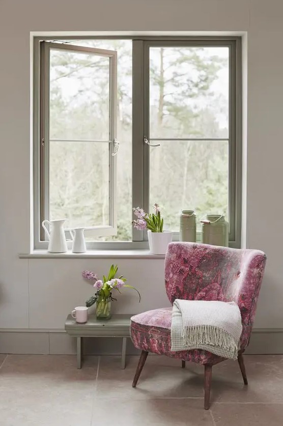 a chic cottage inspired space with a green frame casement window, a green bench and a pink floral chair plus some blooms