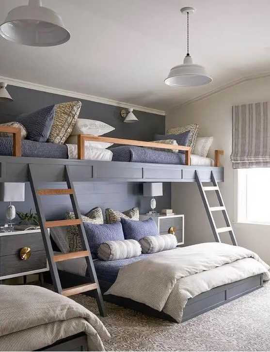 a chic kids' room with built in bunk beds, navy and grey bedding, ladders, elegant nightstands and pendant lamps