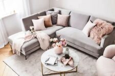 a chic living room with a grey sectional, pink pillows and a pink chair, a grey rug and a round table is a stylish space