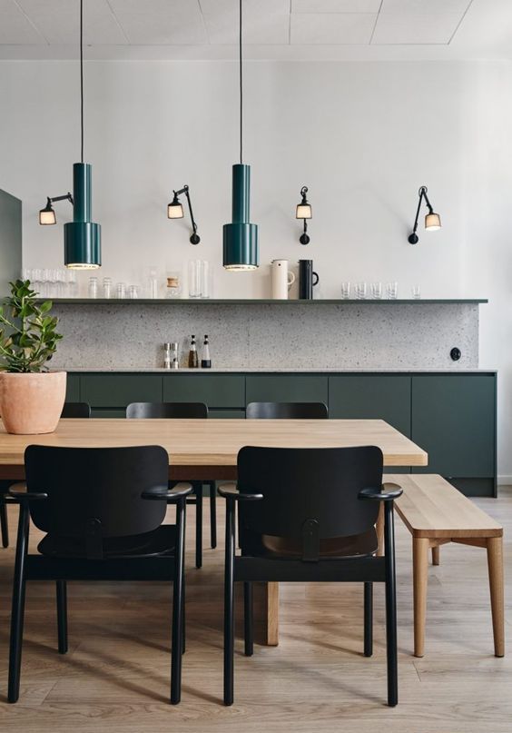 a chic modern kitchen with dark green lower cabinets and an open shelf, a terrazzo backsplash, a dining space with dark green pendant lamps