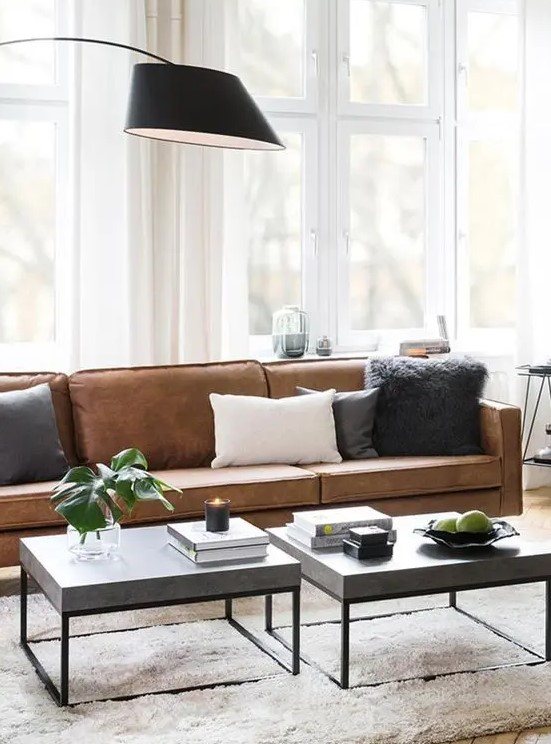 a chic modern living room with a brown leather sofa, grey coffee tables, monochromatic pillows and a black floor lamp