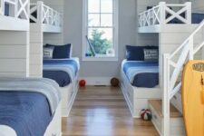 a coastal kids’ bedroom with built-in bunk beds, navy and blue bedding, built-in ladders and a surf