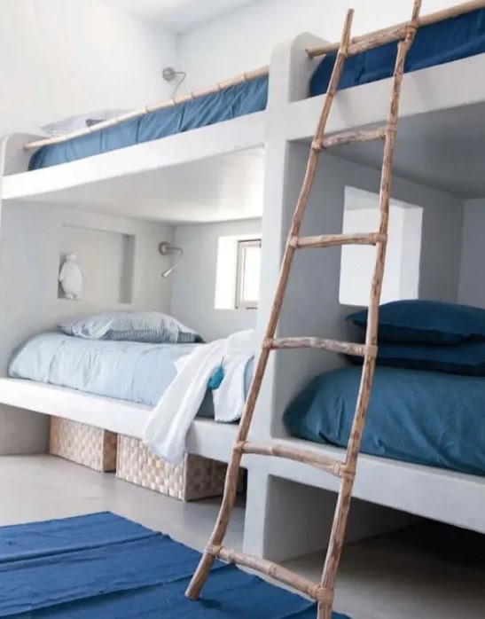 a coastal space with white built in bunk beds, with blue and navy bedding, with a ladder and navy rugs is a stylish space with love to the sea