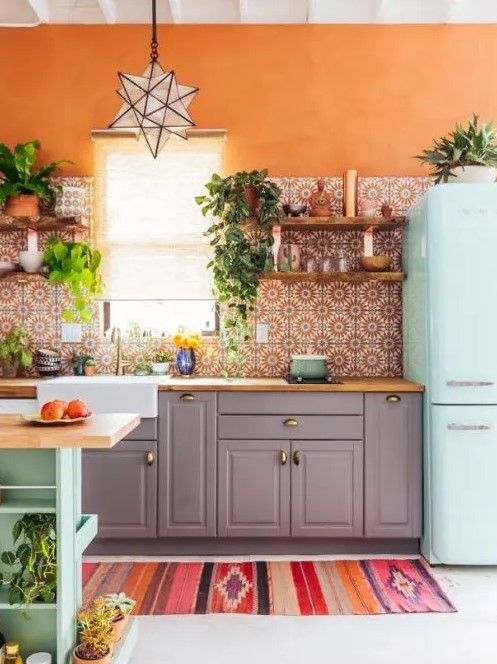 a colorful kitchen with orange walls, grey cabinetry, a mint blue fridge, a matching kitchen island and a bold orange printed tile backsplash