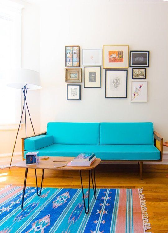 a colorful living room with a turquoise mid century modern sofa and a matching right rug, a hairpin leg table and a gallery wall