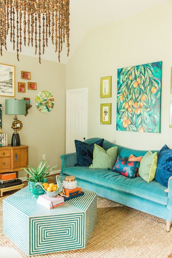 a colorful living room with a turquoise sofa, a bright artwork and a gallery wall, a geo hex shaped table, a bead chandelier