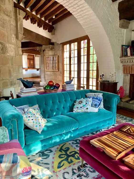 a colorful living room with a turquoise sofa, a bright printed rug, a purple ottoman and colorful pillows is amazing