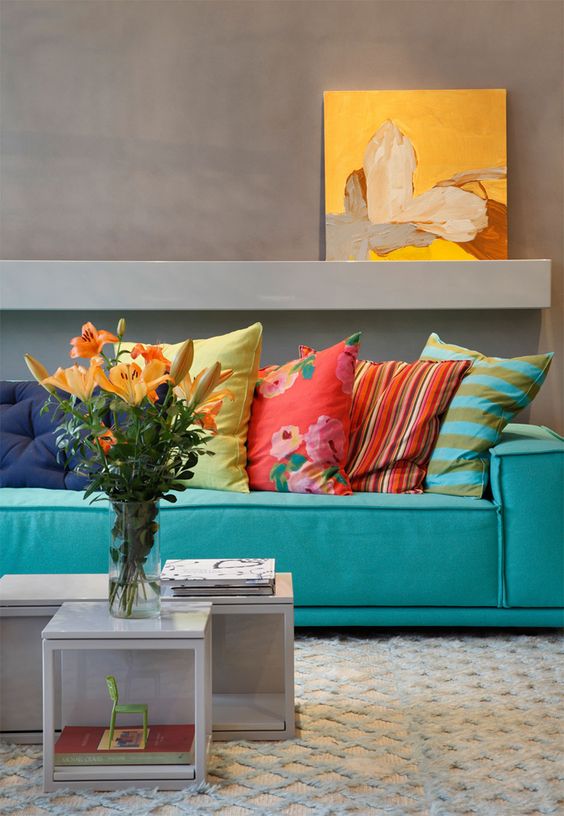 a colorful living room with grey walls, a turquoise sofa with colorful pillows, neutral coffee tables and a bold artwork