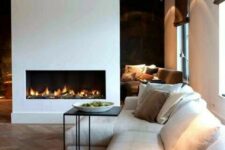 a contemporary living room with a minimalist fireplace, a neutral sofa with lots of pillows, a side table and a rug is a very cozy space