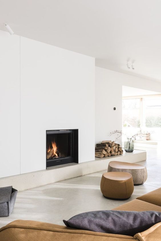 a contemporary living room with a minimalist fireplace, firewood storage, wooden poufs and a sofa plus some pillows