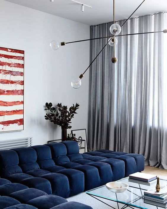 a contemporary living room with a navy low sofa, a glass coffee table, bold artwork and a cool bulb chandelier