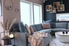 a contrasting living room with a pink and black wall, a grey sectional, a round table and box shelves plus pink pillows
