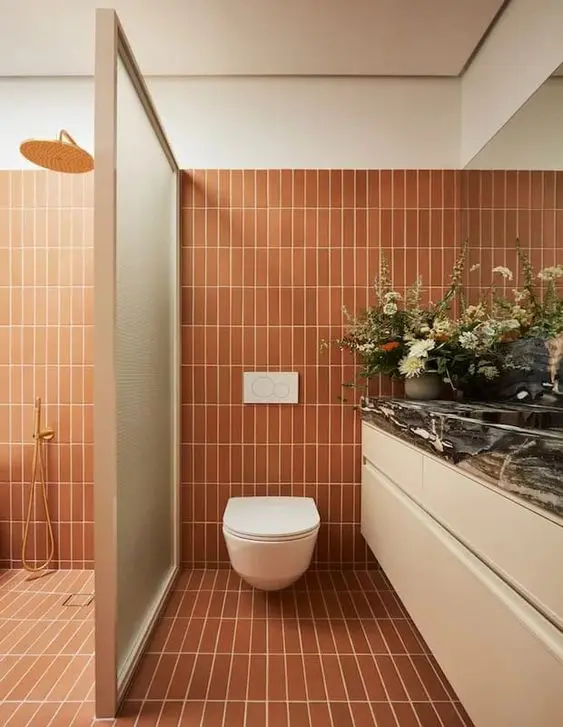 a cool bathroom clad with skinny terracotta tiles, with a shower space, a large vanity and a large mirror is very warm and welcoming