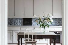 a cool kitchen with a terracotta tile floor, dove grey cabinets, a blue and white tile backsplash and a catchy pendant lamp