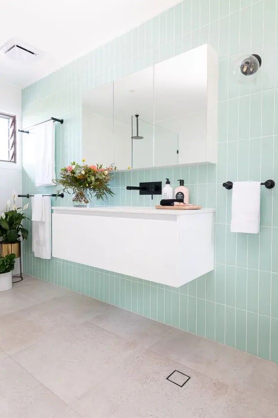 a cool modern bathroom with mint skinny tiles, a white floating vanity, a mirror cabinet and black fixtures for an edgy feel
