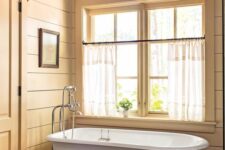 a cottage bathroom with a stained roof, casement windows, a grey clawfoot tub, beadboard walls and a basket