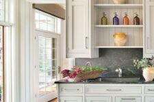 a cottage tan kitchen with beadboard, a grey soapstone backsplash and countertops and stainless steel fixtures