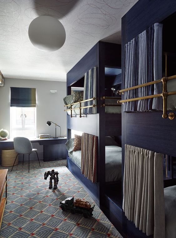 a cozy kids' room with a block of navy bunk beds, a navy desk and a grey chair, a printed rug and some toys