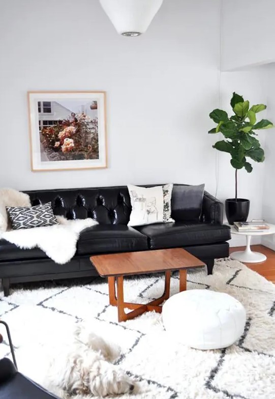 a cozy living room with a black leather sofa, a stained coffee table, a large rug and a white pouf, a potted statement plant