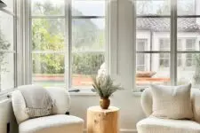 a cozy seating nook with casement windows, neutral chairs, a tree stump side table and neutral curtains is lovely