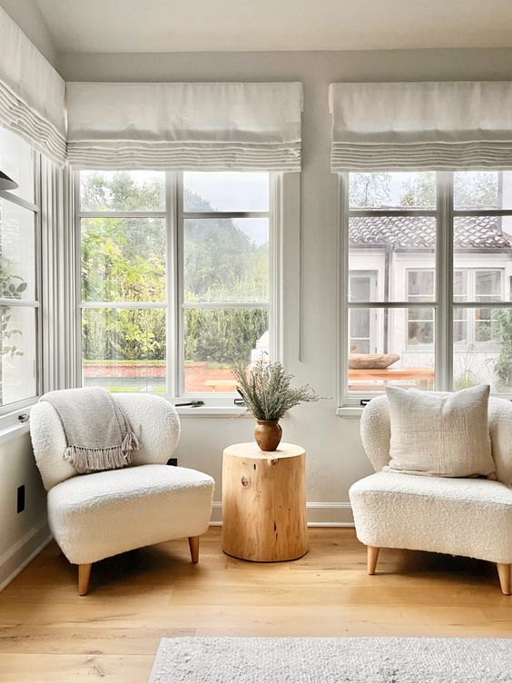 a cozy seating nook with casement windows, neutral chairs, a tree stump side table and neutral curtains is lovely