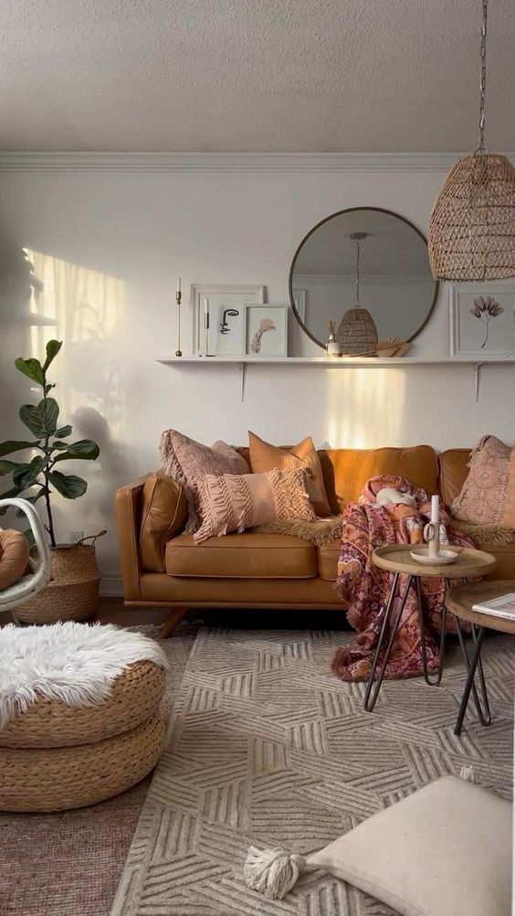 a cozy warm colored boho living room with a tan sofa and pink pillows, hairpin leg tables, a printed rug, jute poufs and a woven pendant lamp