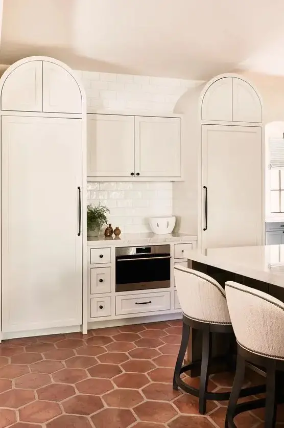a creamy kitchen with curved cabinets, a large kitchen island with a seating zone and a terracotta tile floor that adds interest and texture