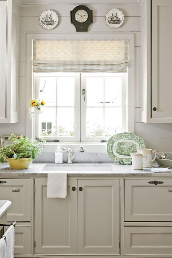 a creamy ktichen with shaker cabinets, beadboard walls, a casement window, grey countertops and vintage plate decor