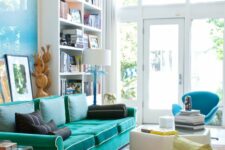 a double-height living room with a tall bookcase, a turquoise sofa, a coffee table, a blue chair with a footrest
