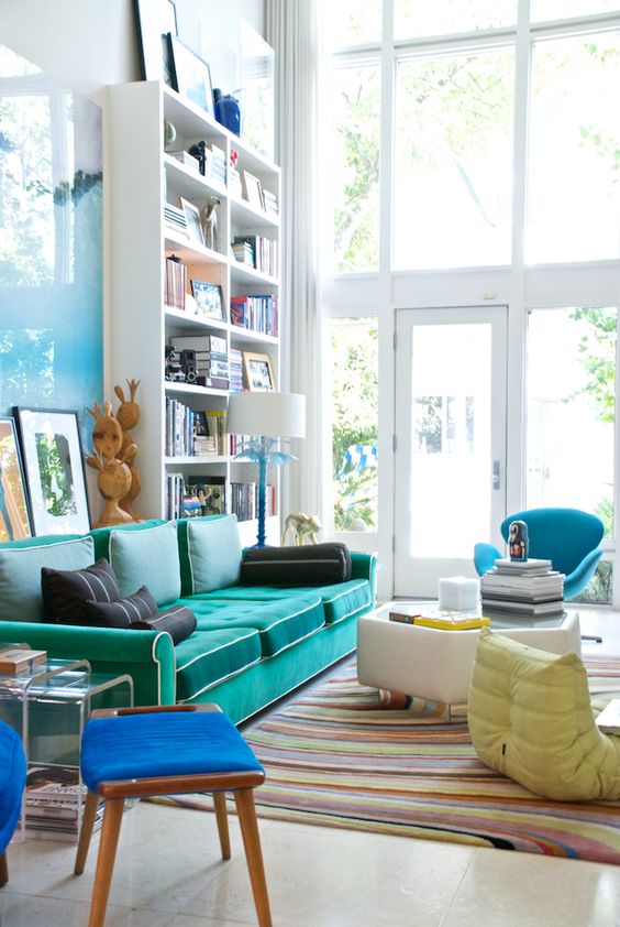 a double-height living room with a tall bookcase, a turquoise sofa, a coffee table, a blue chair with a footrest