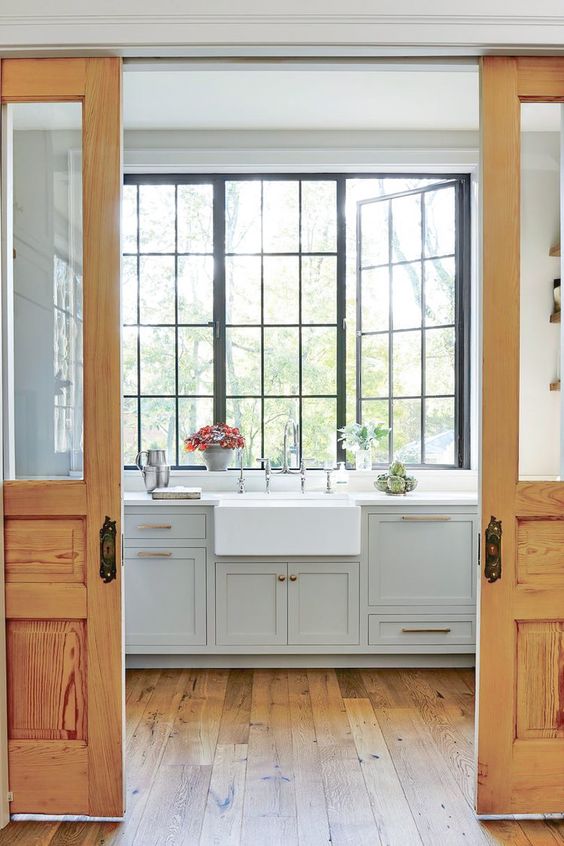 a dove grey farmhouse kitchen with shaker cabinets and white countertops, tall black casement windows