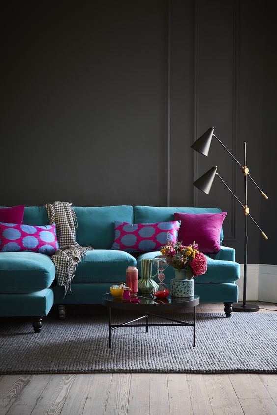 a dramatic living room with a turquoise sofa and bright pillows, a round coffee table, black lamps and a dark rug