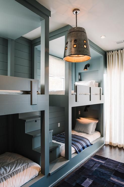 a dreamy blue kids' room with multiple bunk beds and printed bedding, a bold printed rug, neutral curtains and a metal lamp