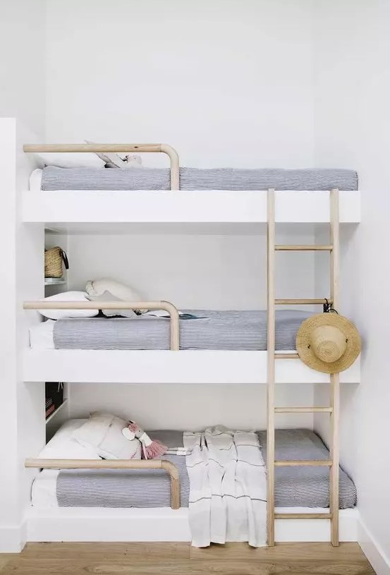 a dreamy coastal sleeping nook with a triple bunk bed, navy and white bedding, wooden ladders and a straw hat looks dreamy