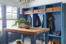 a farmhouse entryway with a blue clothes rack with seats, blue walls and a matching dog kennel with a butcherblock countertop