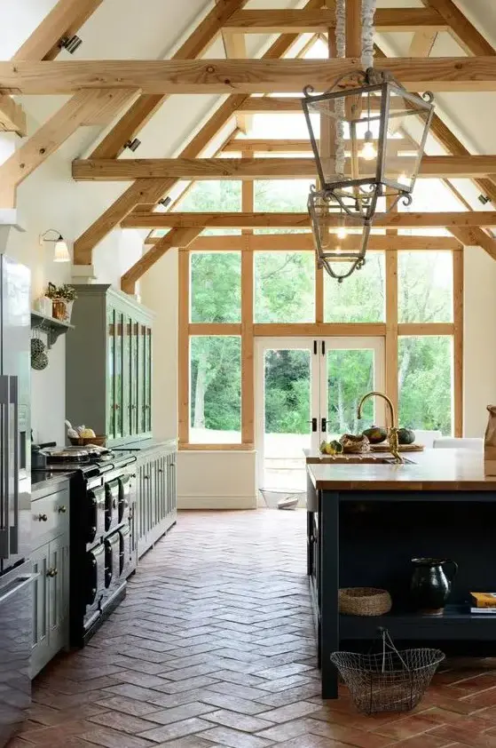 a farmhouse kitchen with a terracotta tile floor, blue cabinets, a navy kitchen island, a black cooker, wooden beams and pendant lamps