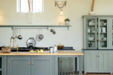 a farmhouse kitchen with a terracotta tile floor, grey cabinetry, a graphite grey kitchen island, wooden beams and pendant lamps