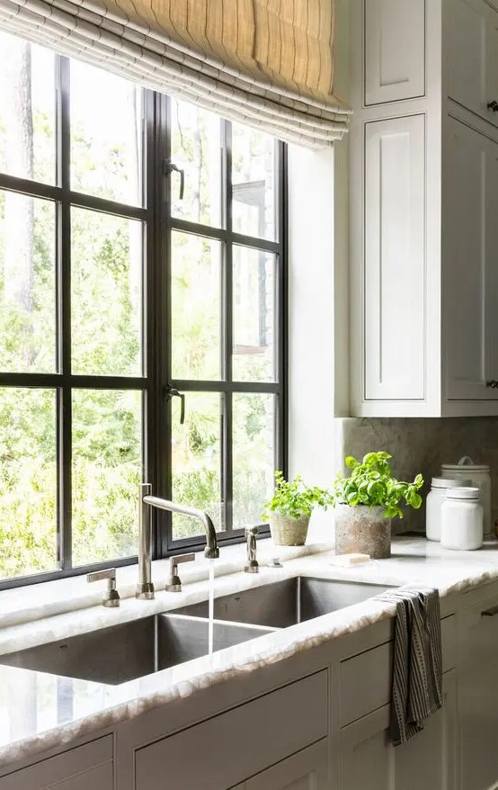 a farmhouse kitchen with shaker style cabinets, a stone countertop, a black frame casement window and striped curtains