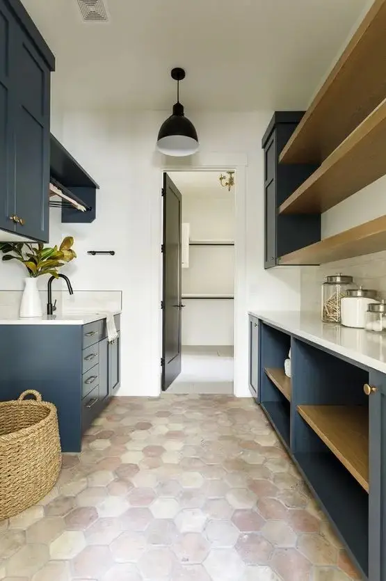 a farmhouse laundry with a terracotta tile floor, navy cabinets, white countertops, open shelves and a basket is very cozy