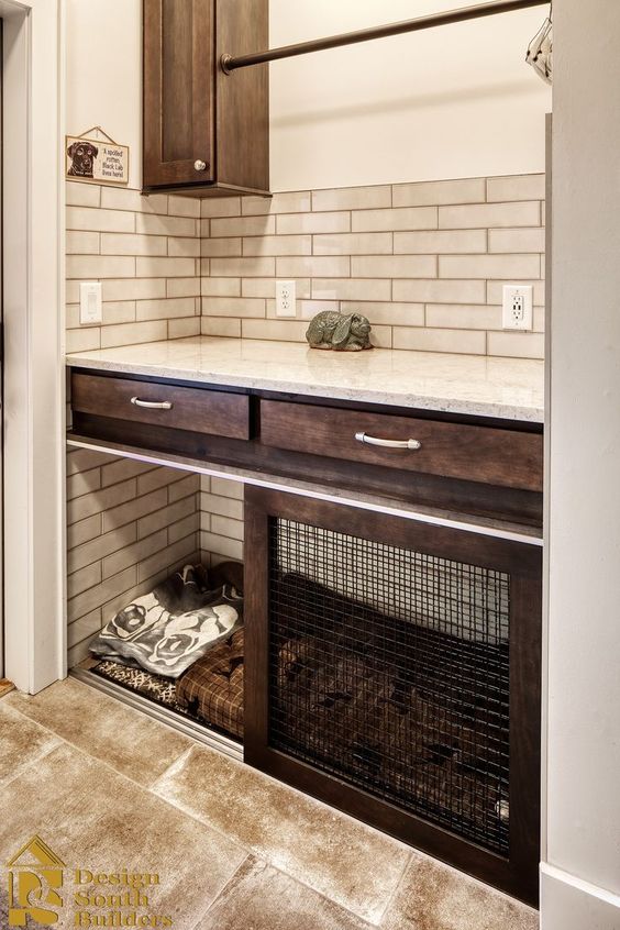 a farmhouse mudroom with dark-stained cabinets, neutral tiles, a built-in dog crate with blankets plus a sliding door